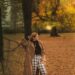a woman is walking through a park in the fall