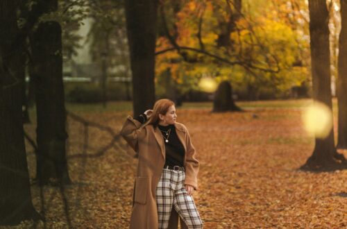 a woman is walking through a park in the fall