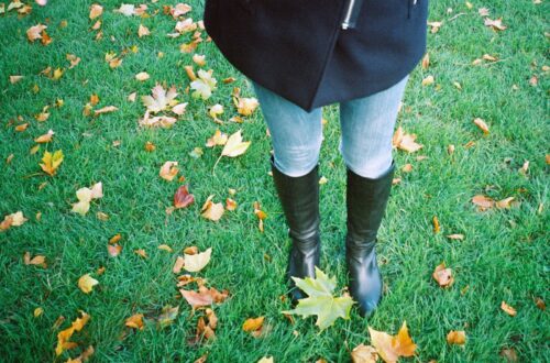 person in black jacket and blue denim jeans standing on green grass field